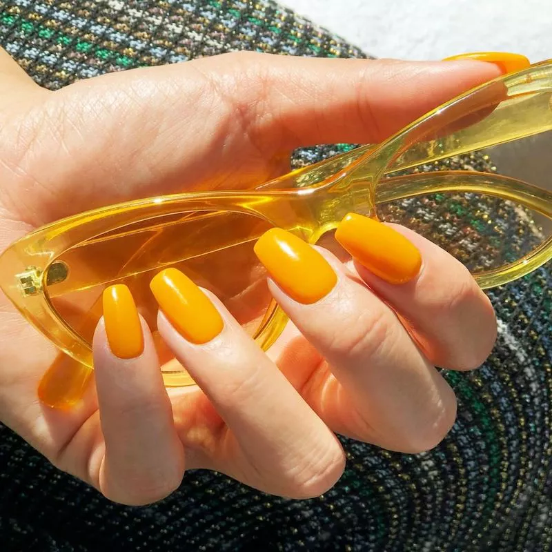 Yellow dip powder nails holding sheer yellow sunglasses