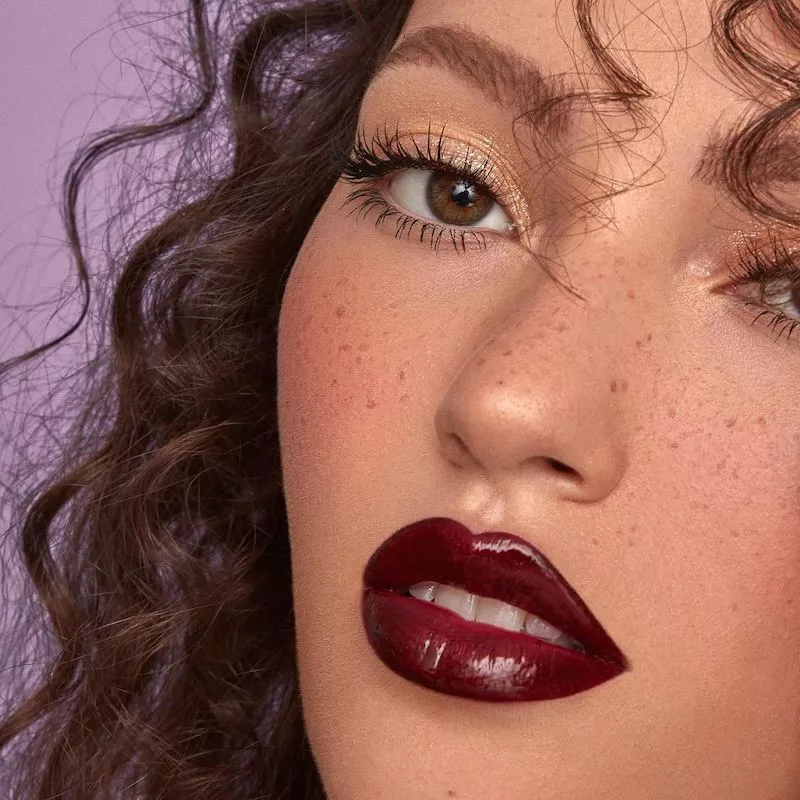 Model with brushed brows, subtle gold shimmer eye makeup, and burgundy lipstick