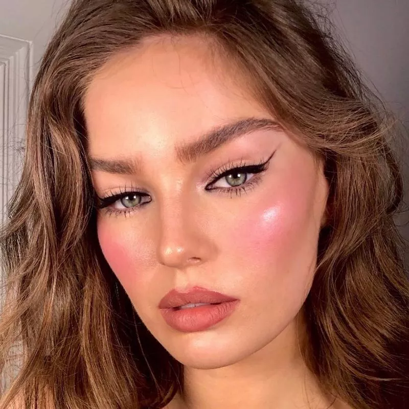 Model with extended winged eyeliner, rose-toned lips, and radiant blush