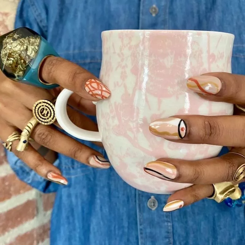 Hands with abstract evil eye manicure holding coffee mug