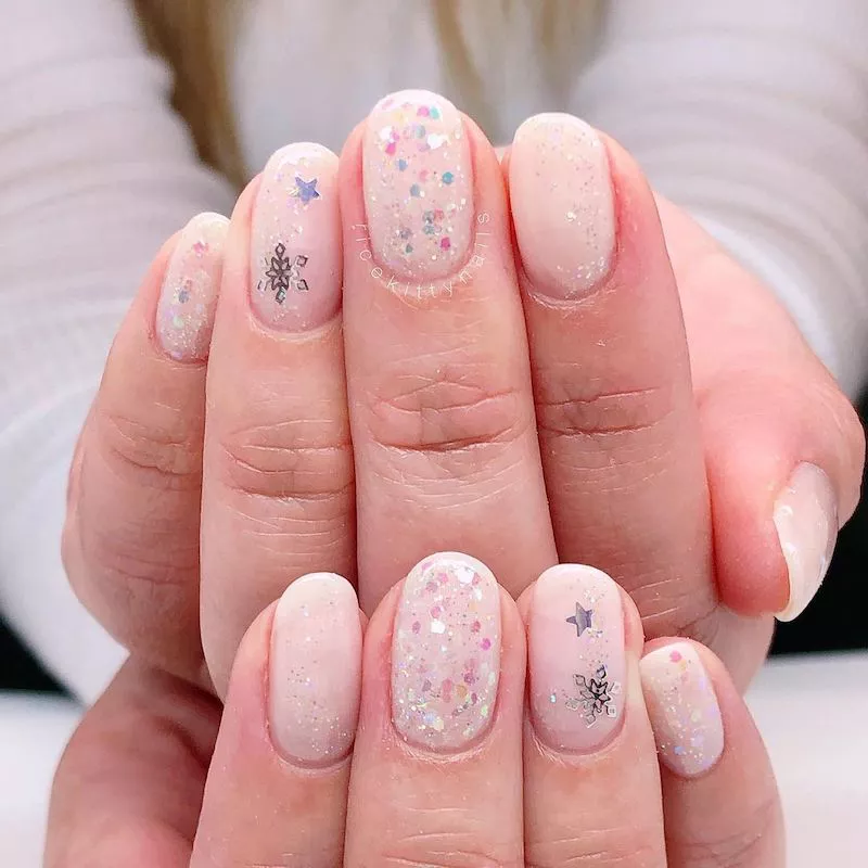 Pale pink nails with silver snowflake decals and confetti sparkles
