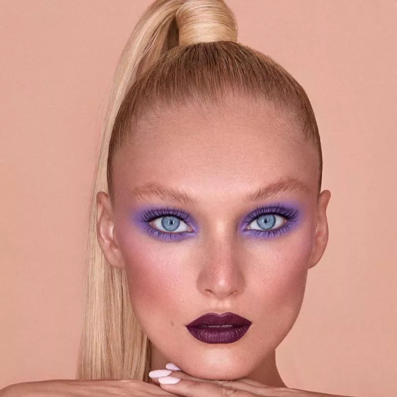Model with high blonde ponytail, lavender eyeshadow, and burgundy lipstick