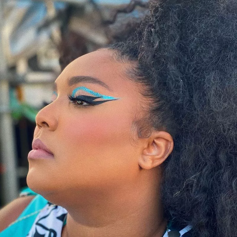 Lizzo wears a graphic eye look with black double cat eye and teal shimmer floating eyeliner