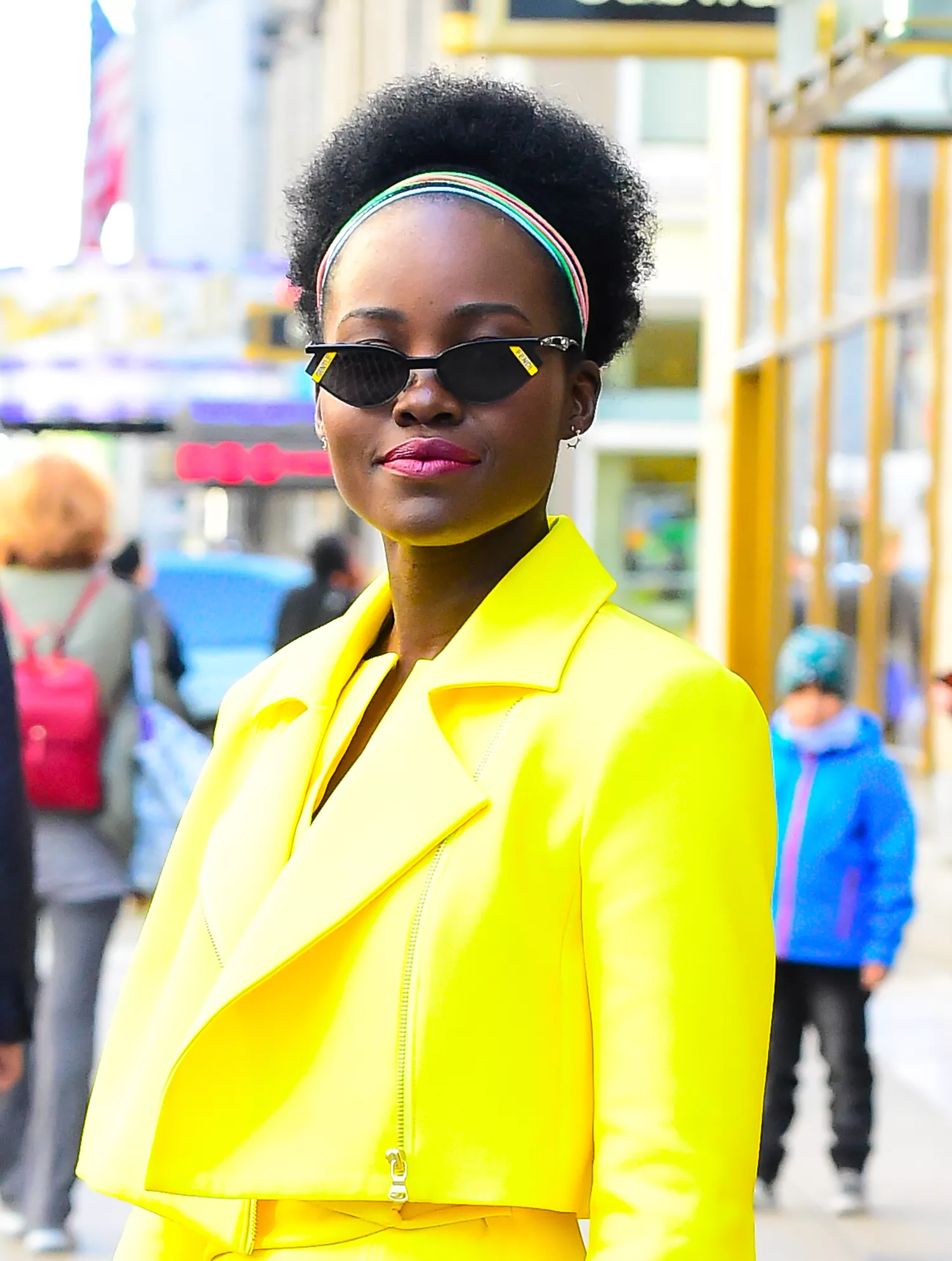 Lupita Nyong'o in Midtown New York wearing a yellow suit and magenta lipstick