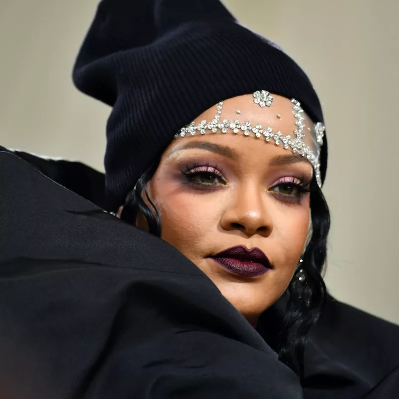 Rihanna wears purple eyeshadow, burgundy lipstick, and a black beanie to the Met Gala