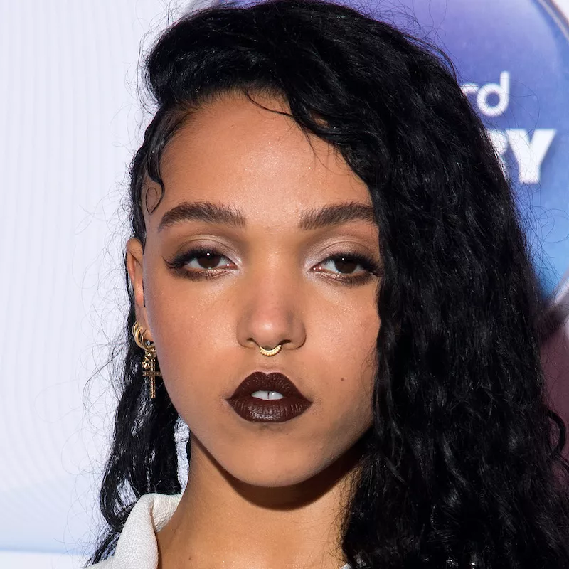 FKA Twigs wears opaque black lipstick, subtle eye makeup, curly hair, and gold jewelry