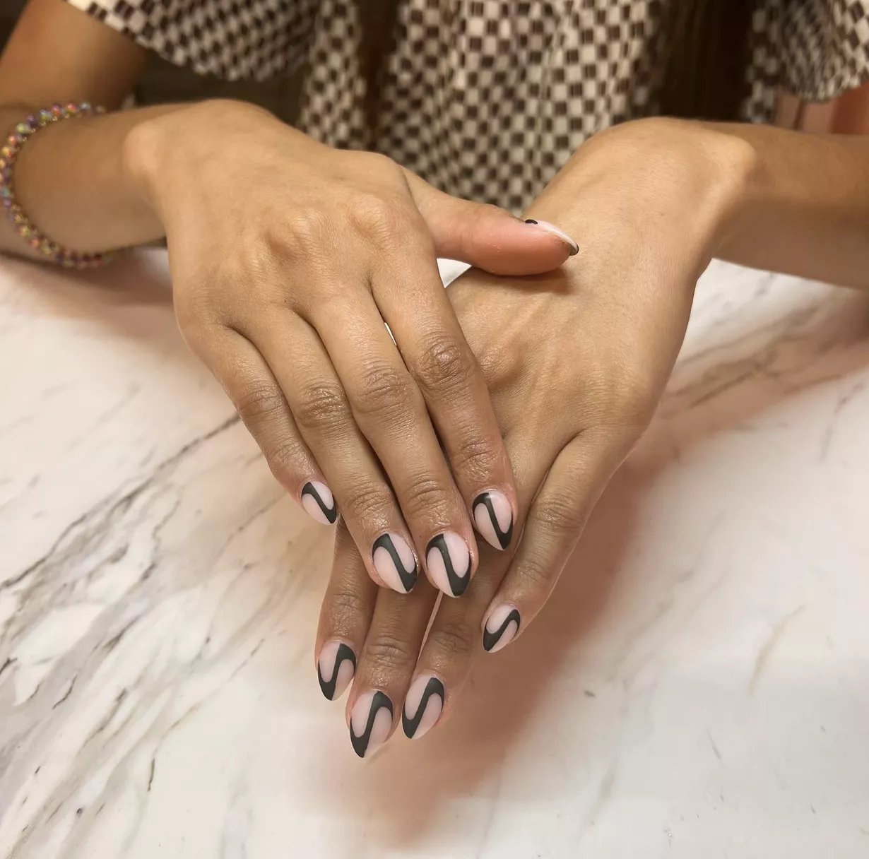 Manicured crossed hands with dip powder nails in geometric op-art pattern