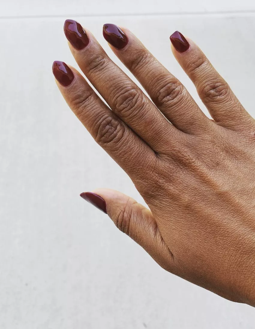 Pointed burgundy dip powder nails on a white background