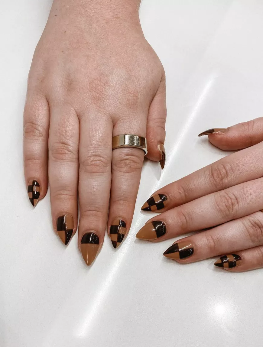 Manicured hand with brown and black checkerboard dip powder nails against white backdrop