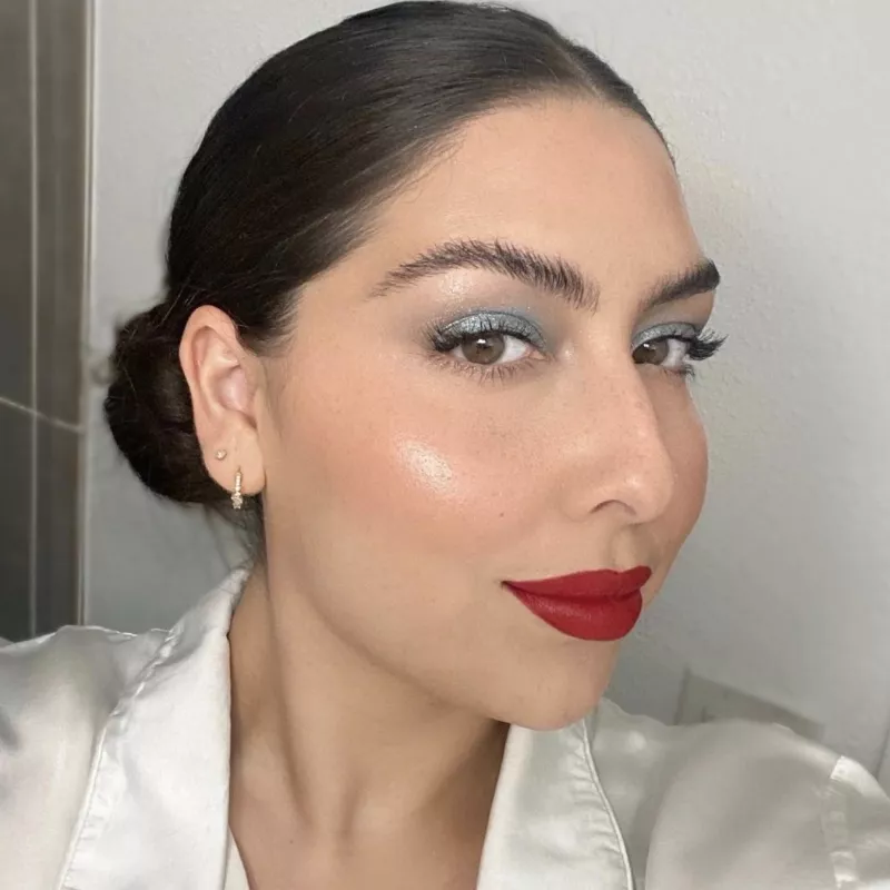 Woman with metallic blue glitter eyeshadow, subtle highlighter, and red lipstick
