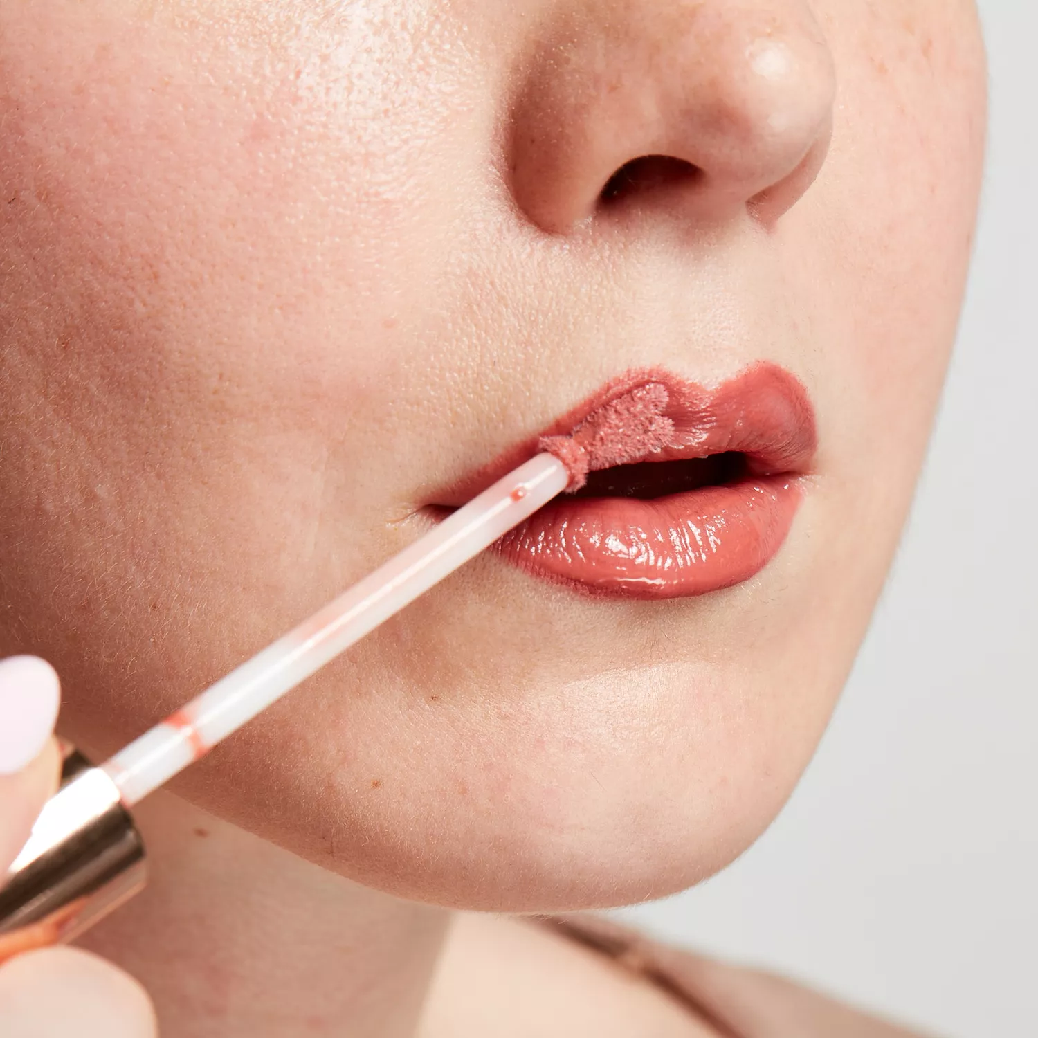 Close up of a woman topping off her lipstick with lip gloss