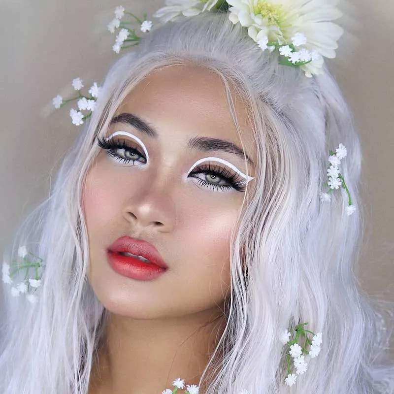 Makeup artist with white graphic eyeliner, radiant makeup, and white hair with flowers
