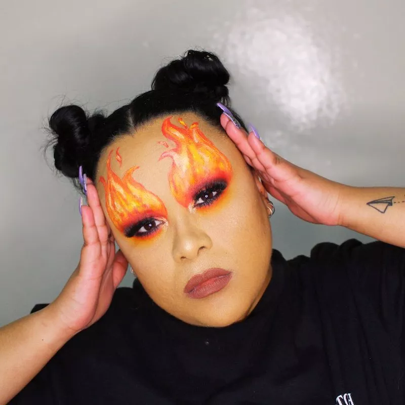 Makeup artist with yellow and orange flame makeup look and high space bun hairstyle