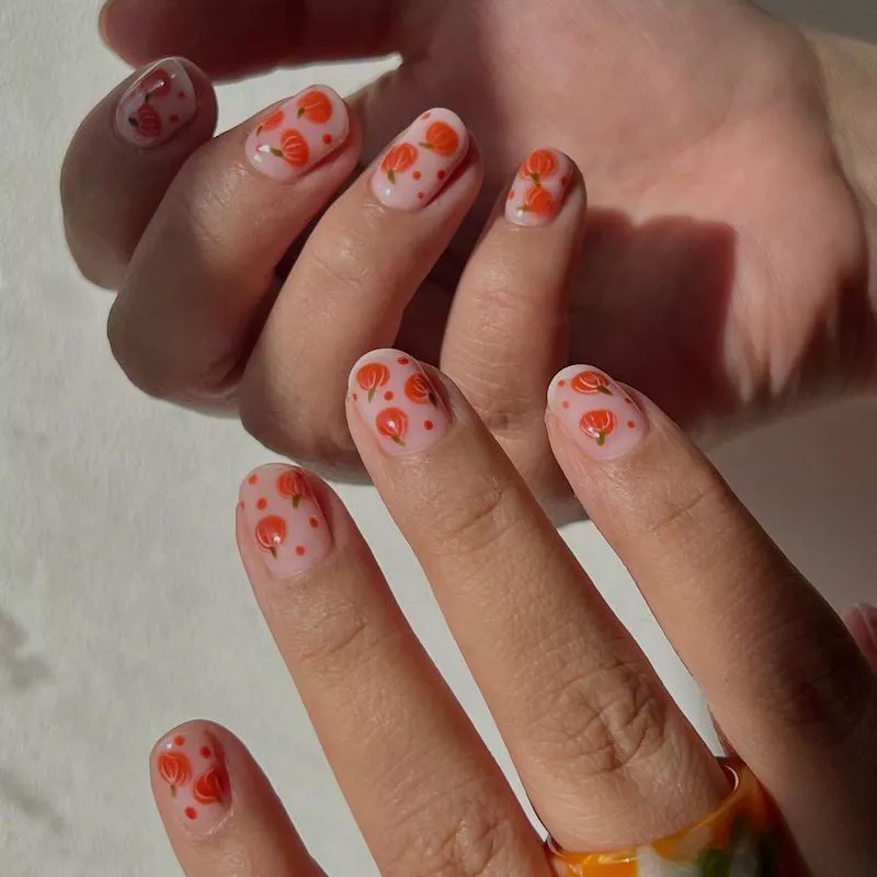 Neutral manicure with small pumpkin nail designs and orange polka dots