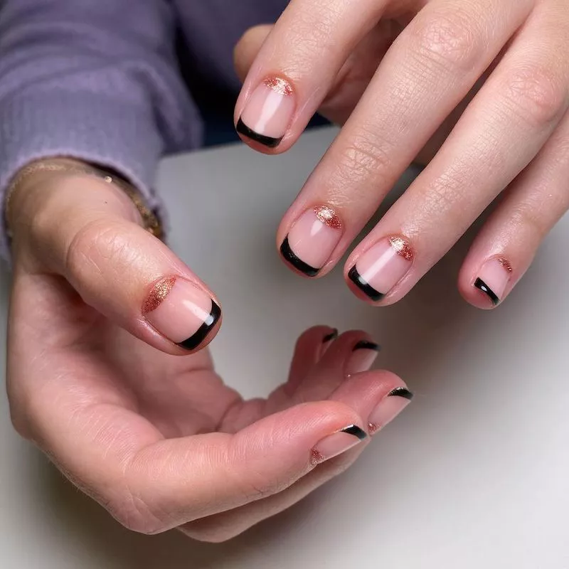 Black French manicure with gold sparkle half-moon nail design at cuticle