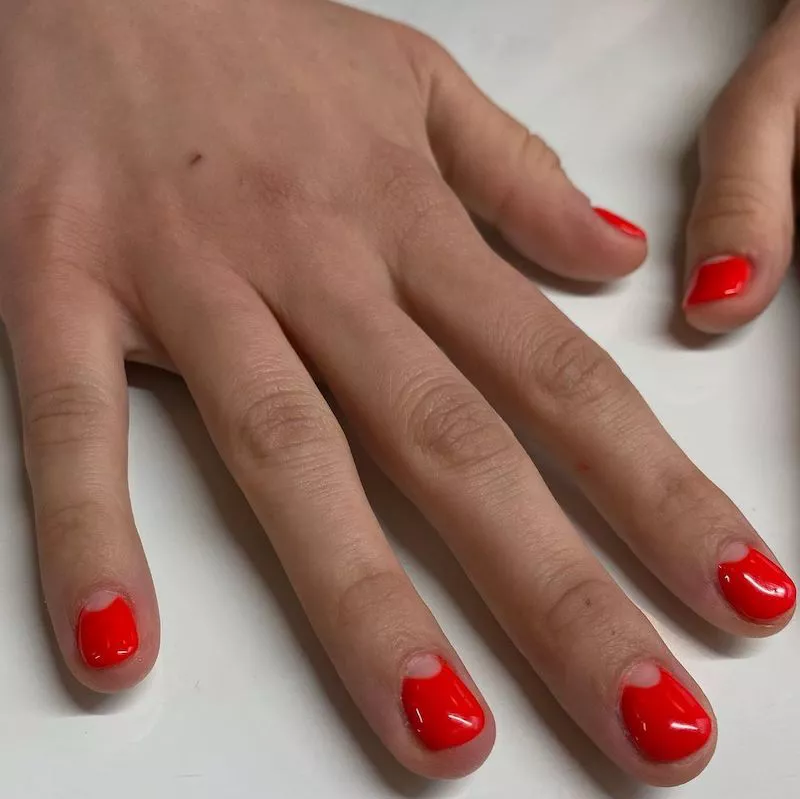 Red-orange manicure with negative space half-moon nail design