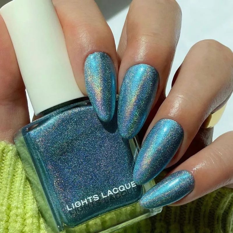 Long almond nails with blue glitter polish holding bottle