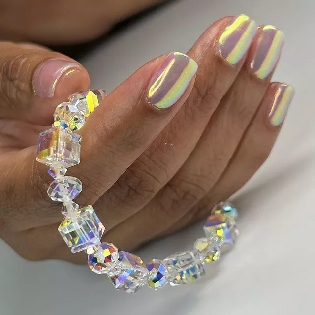 Hand with iridescent gel manicure holding a crystal bracelet
