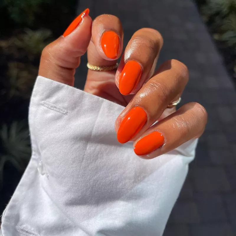 Solid orange glossy manicure against white shirt sleeve