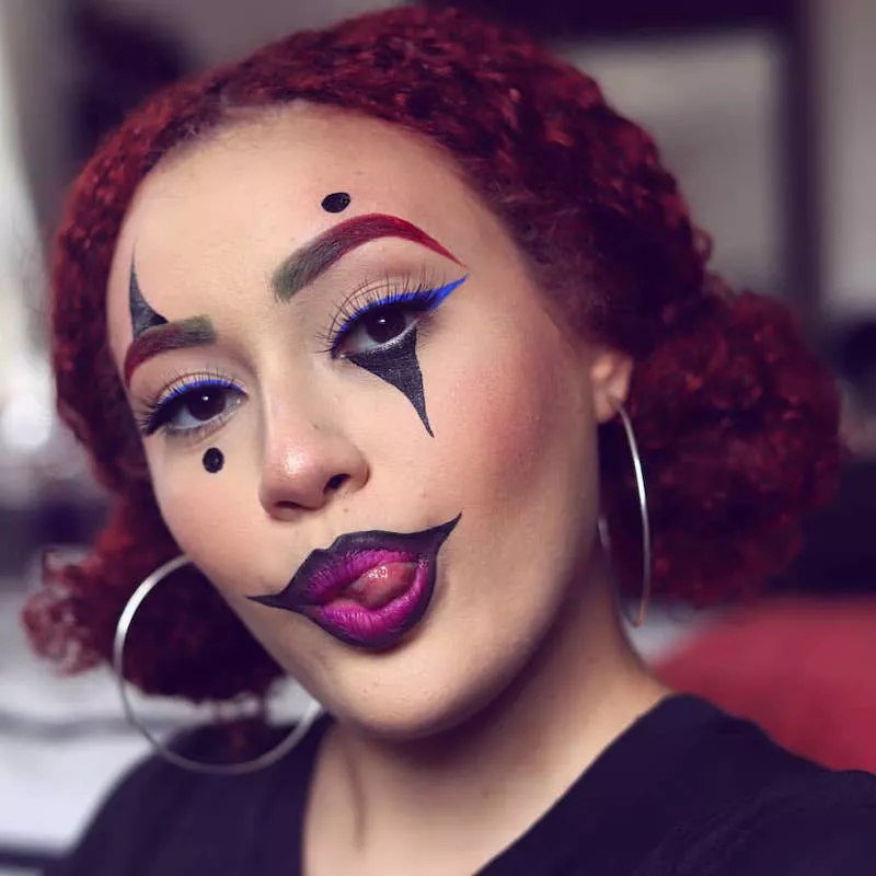 Woman wears clown-inspired makeup, blue winged eyeliner, and red curly low buns