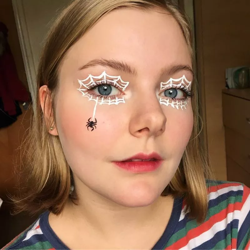 Makeup artist wears white spider web eye makeup with spider design on cheek