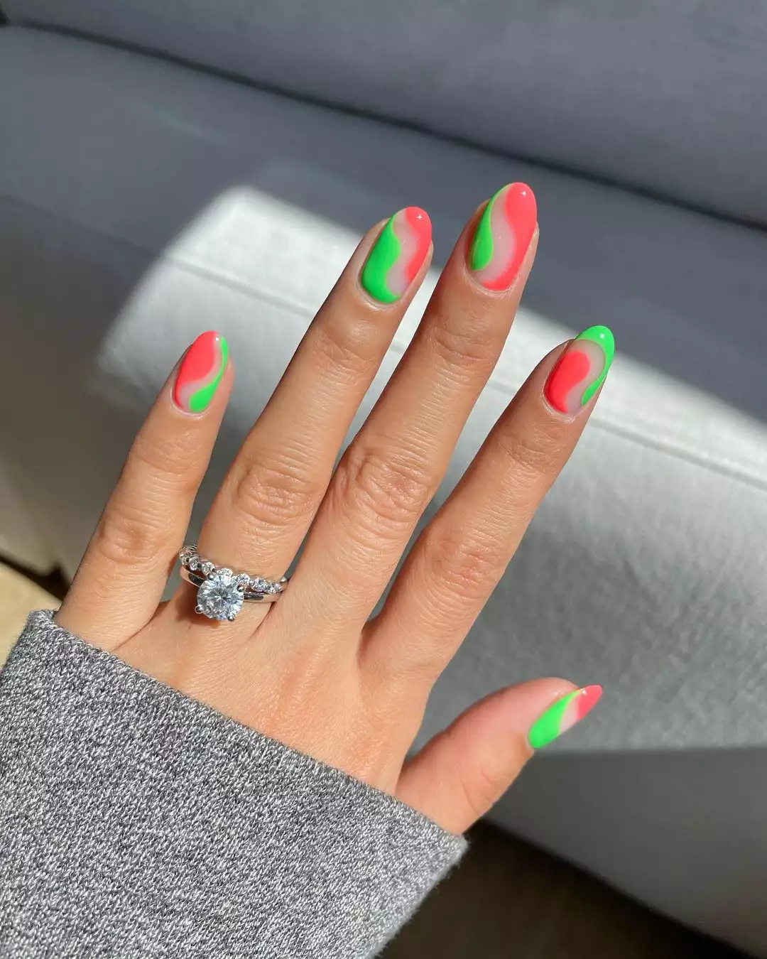 Person's hand with neon pink and green swirl nails.