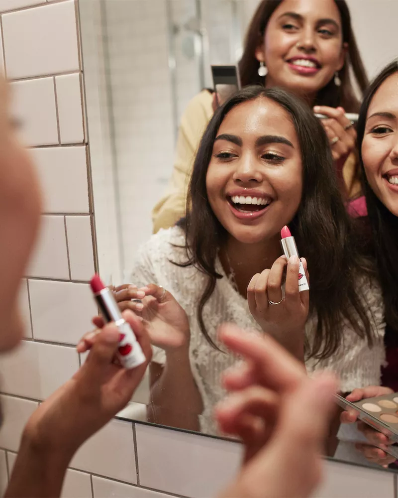 girls doing makeup together in bathroom mirror