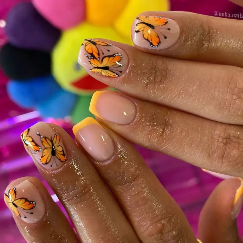 Neutral nails with orange butterfly designs and pale orange baby French accent tips