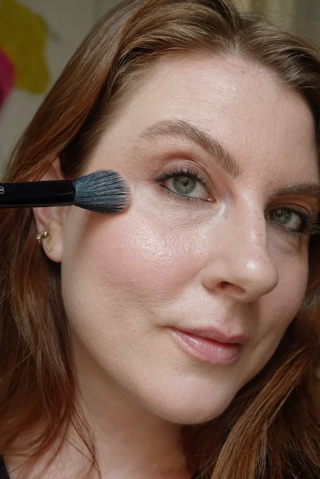 Makeup artist and Byrdie writer Ashley Rebecca applies highlighter to cheekbones with a brush