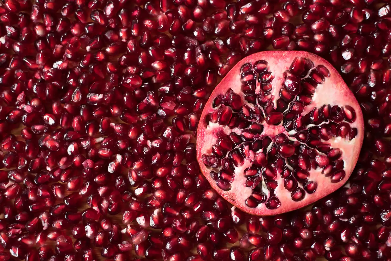 A full frame photo of pomegranate seeds, with half of a cut pomegranate. 