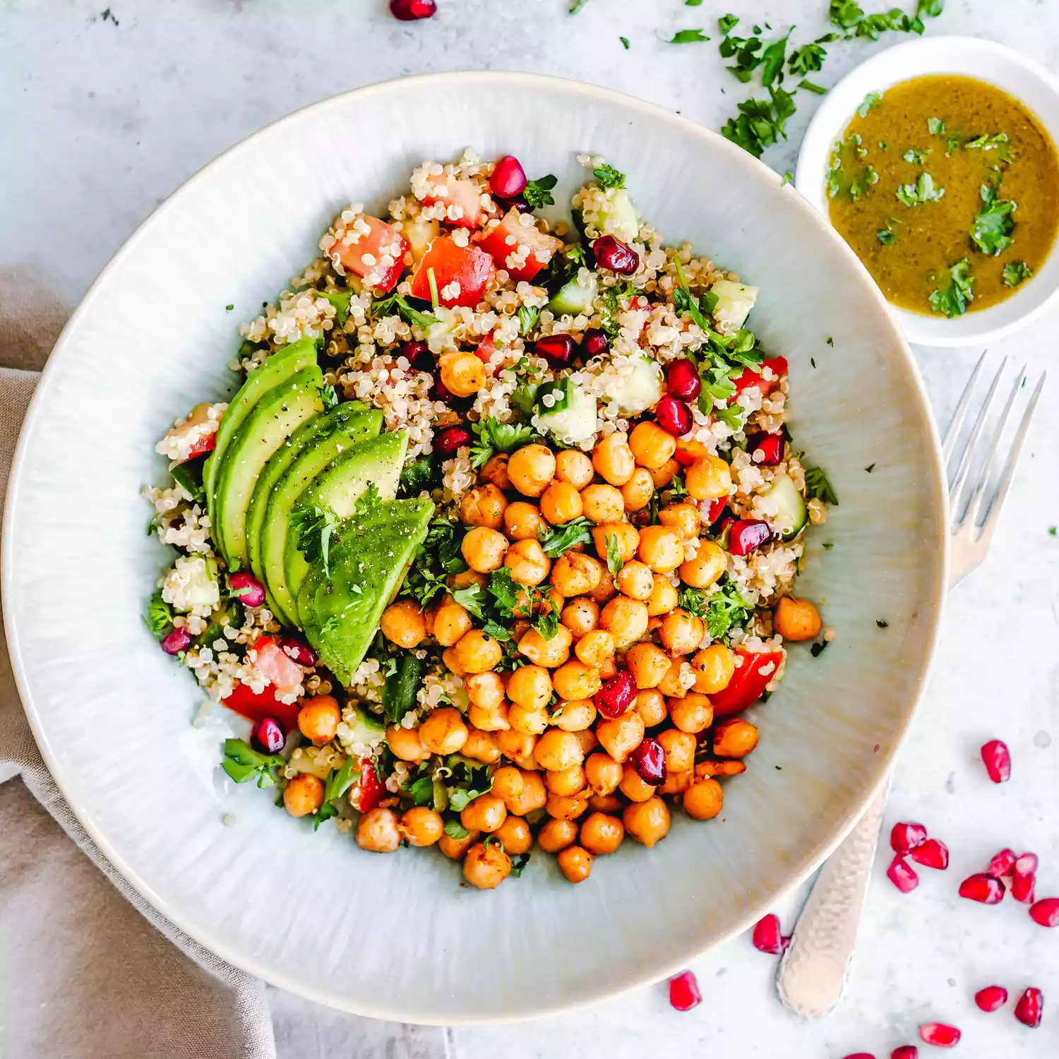 A bowl of chickpea salad with quinoa and avocado. Dressing on the side.