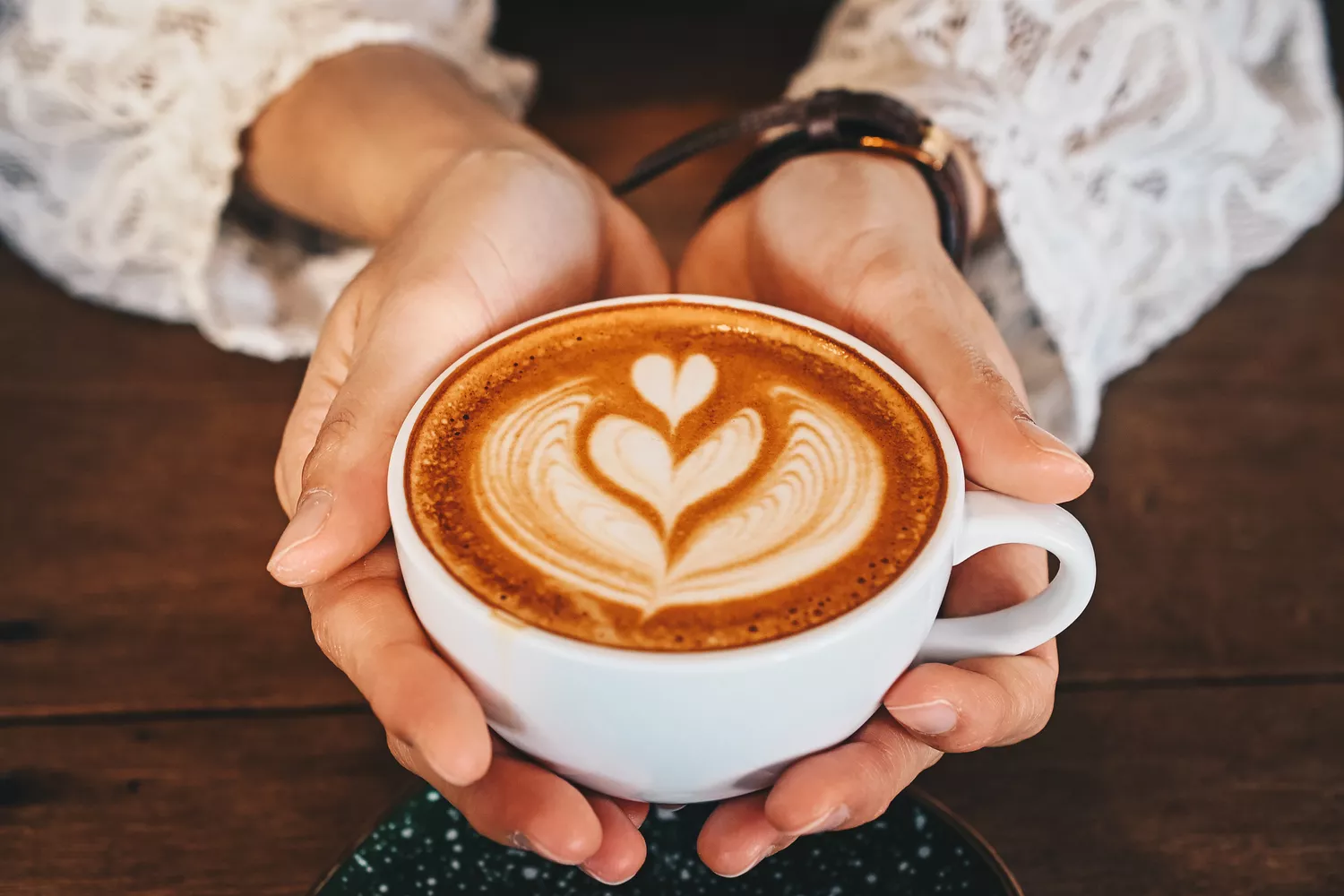 Cropped shot of woman hands holding a cup of hot latte coffee in her hands
