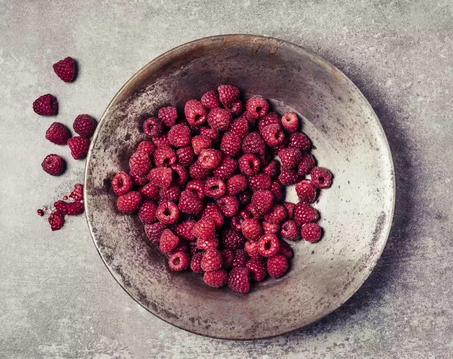 A large ceramic bowl full of raspberries sits atop a table.