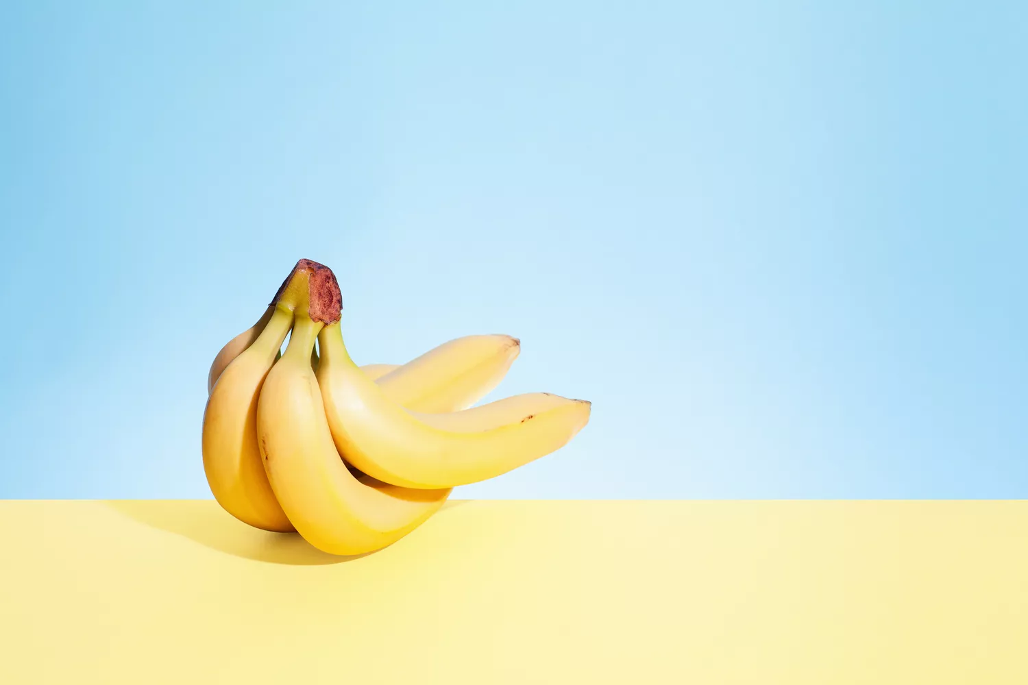 A bunch of bananas against a pale blue and pale yellow backdrop.