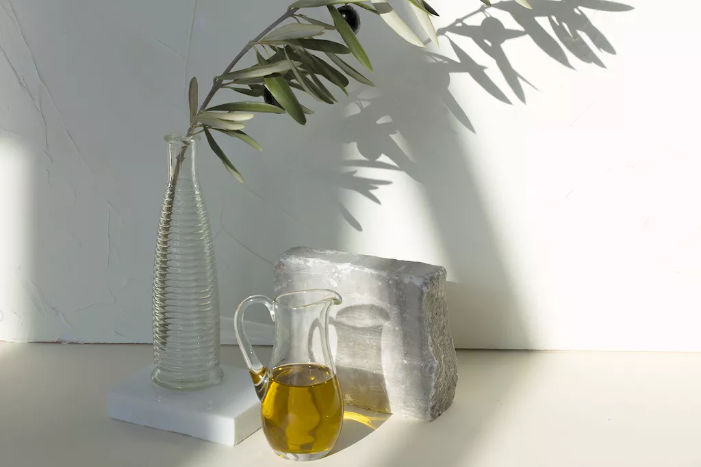 Olive oil in a pitcher and an olive branch in a vase