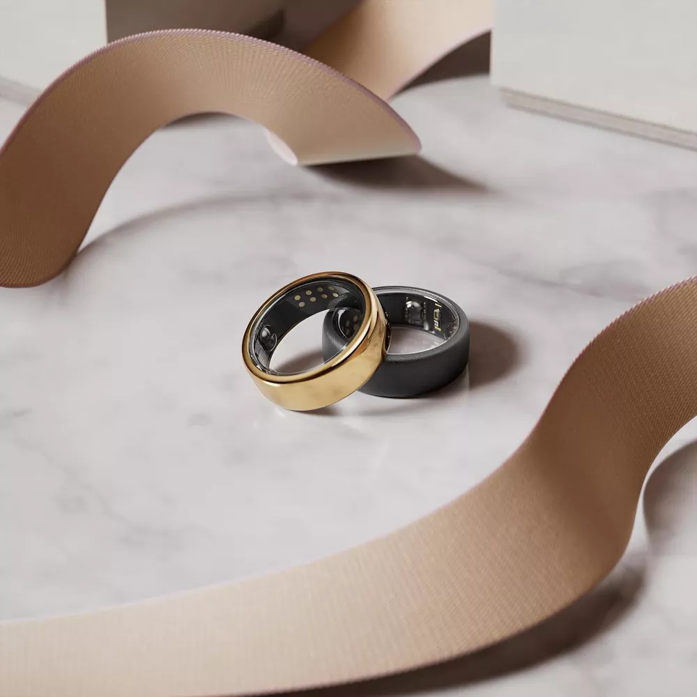 Two Oura smart rings, one gold and one gray, on marble table