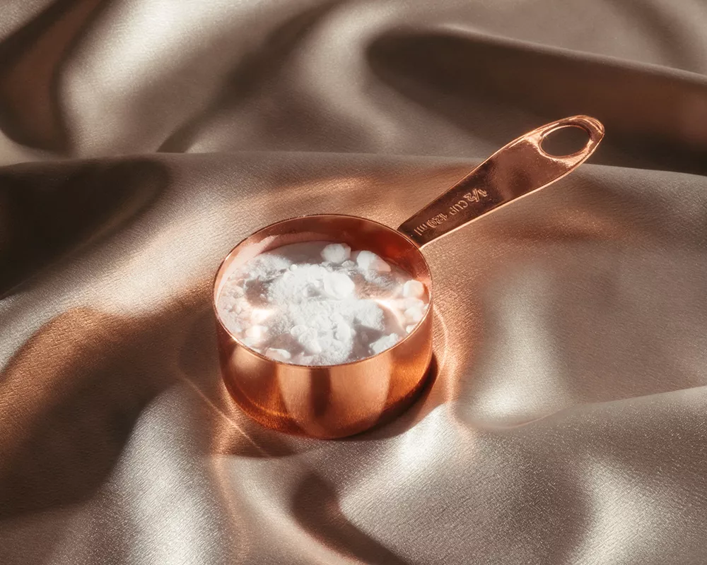 Baking soda in a copper measuring cup, on champagne-colored silk.