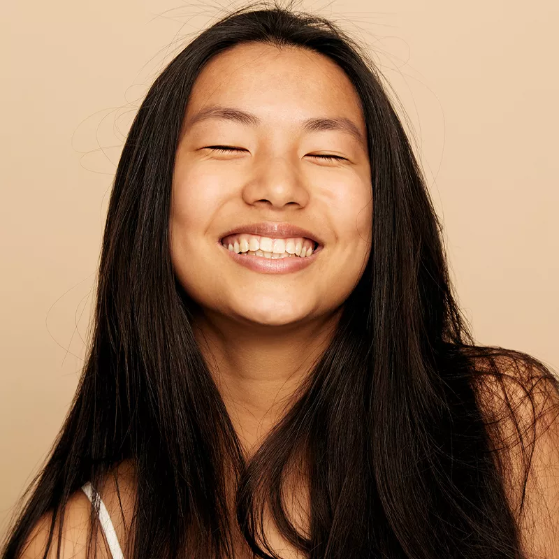 woman with long black hair smiling on a tan background