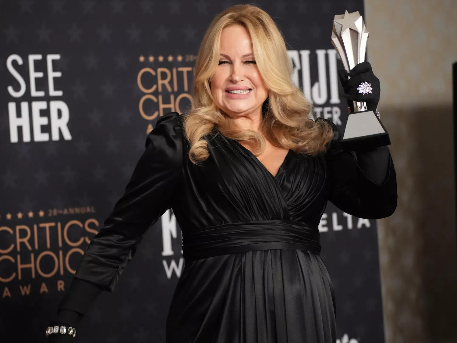 Jennifer Coolidge holds her 2023 Critics Choice award while wearing a black gown and opera gloves