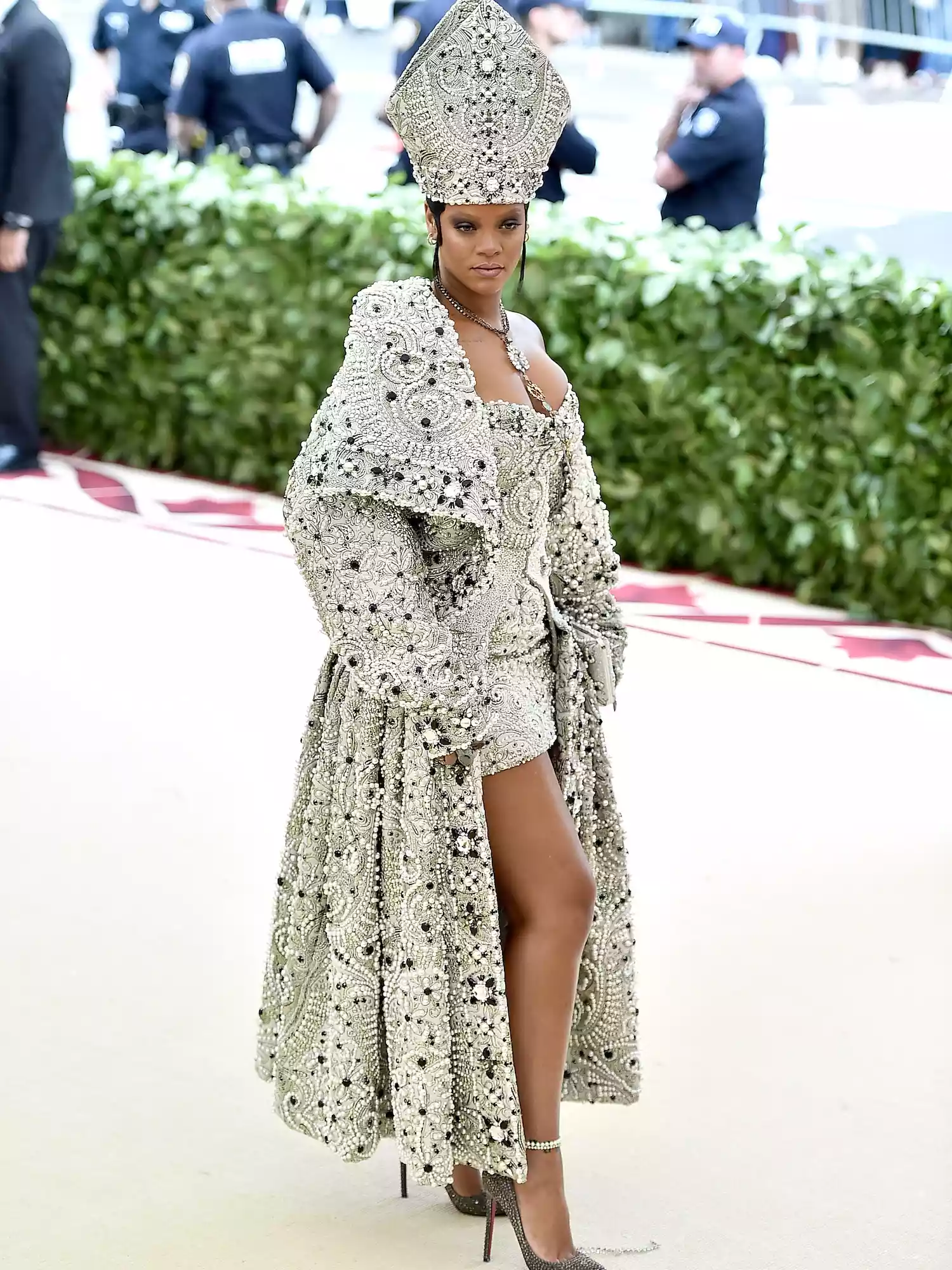 Rihanna wears a Maison Margiela mini dress, coat, and cardinal hat to the 2018 Met Gala