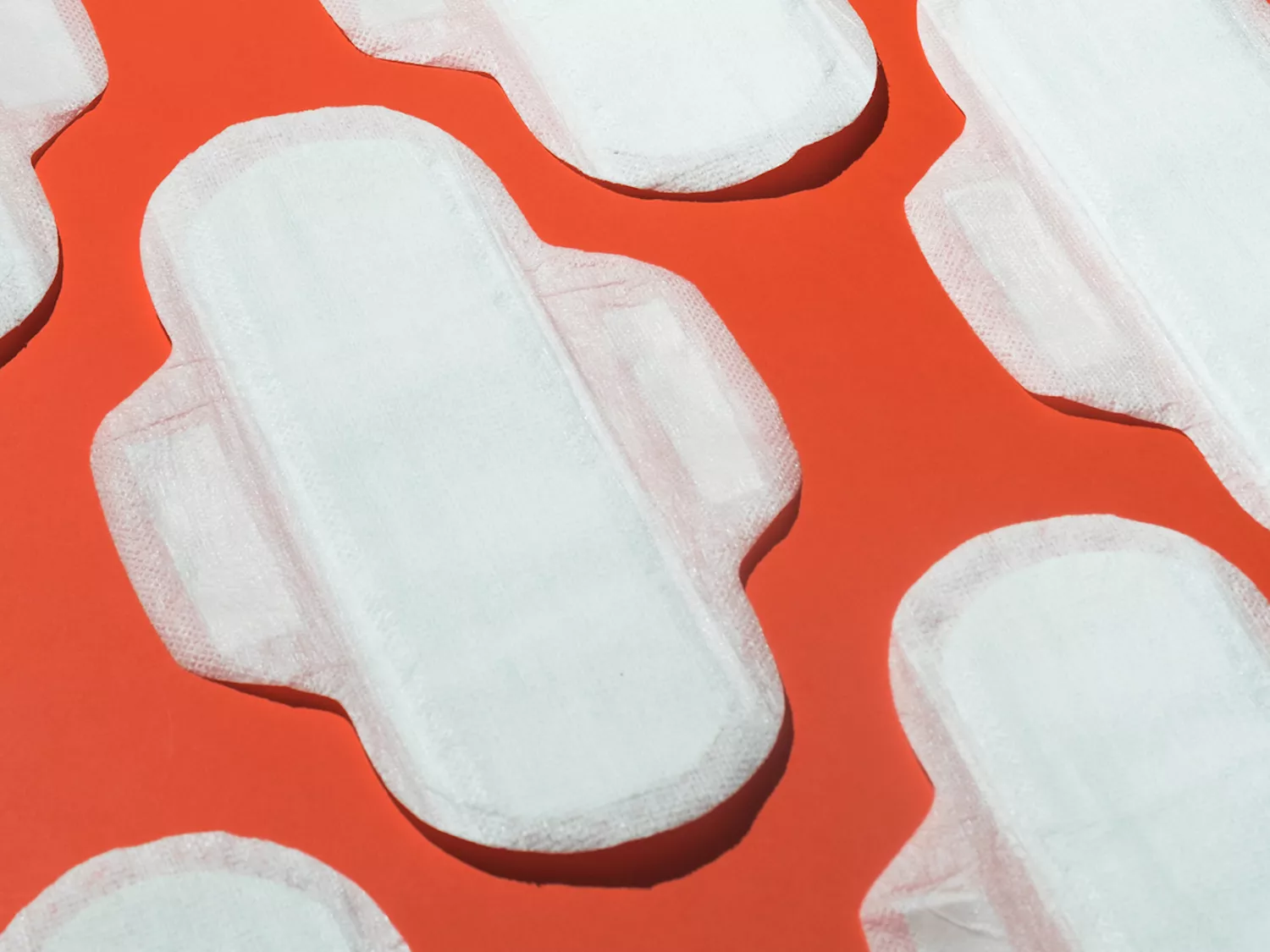 Several clean white menstrual pads on orange background