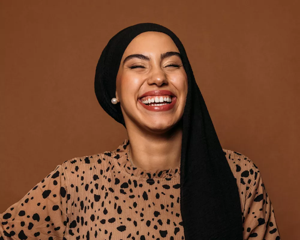 Portrait of a smiling woman in a camel-colored Dalmatian print top.