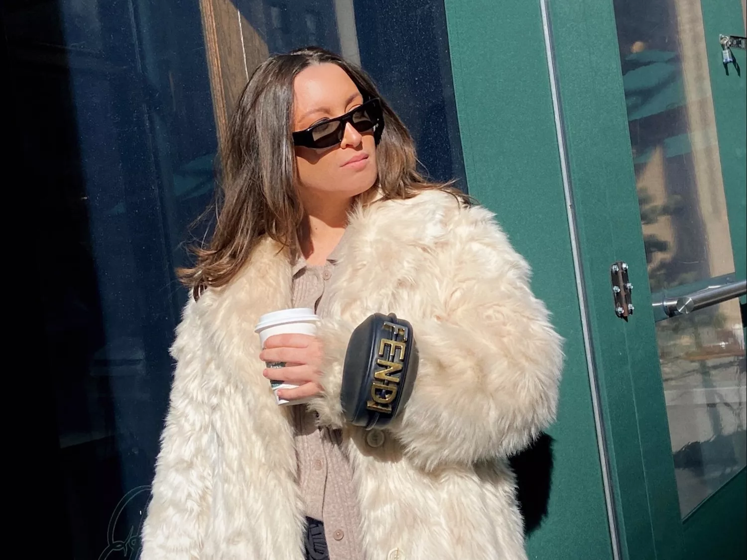 Byrdie writer Bella Gerard wears a black Fendi bracelet bag, sunglasses, and cream fur coat