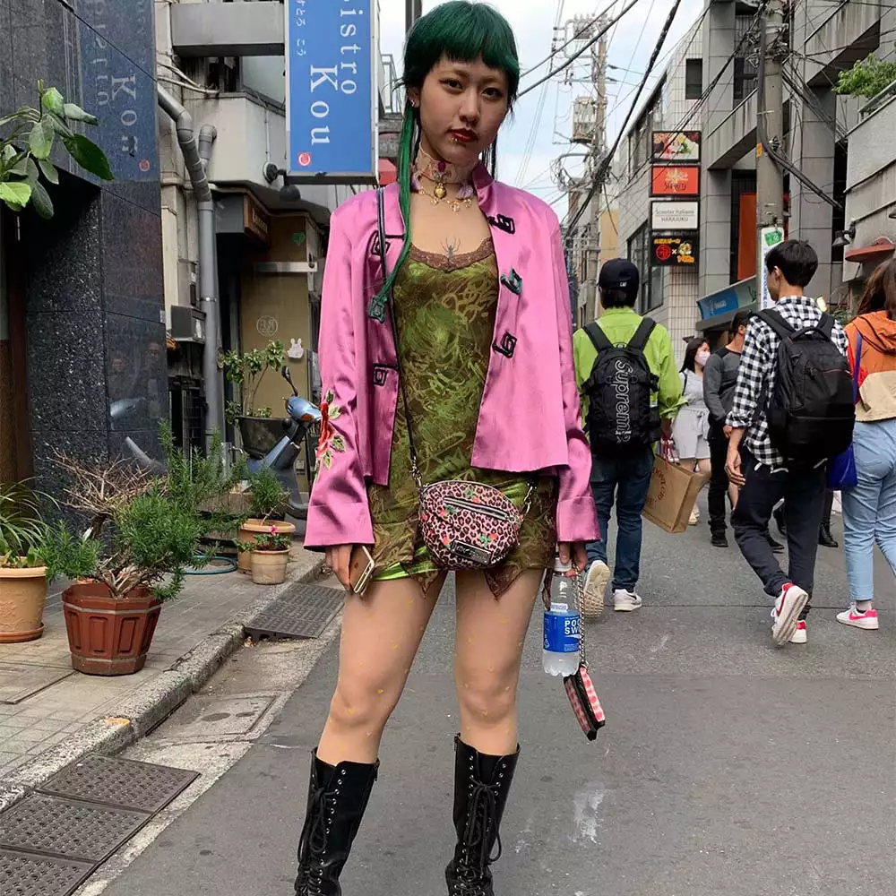 Woman with green hair wearing a pink jacket and green mini dress.