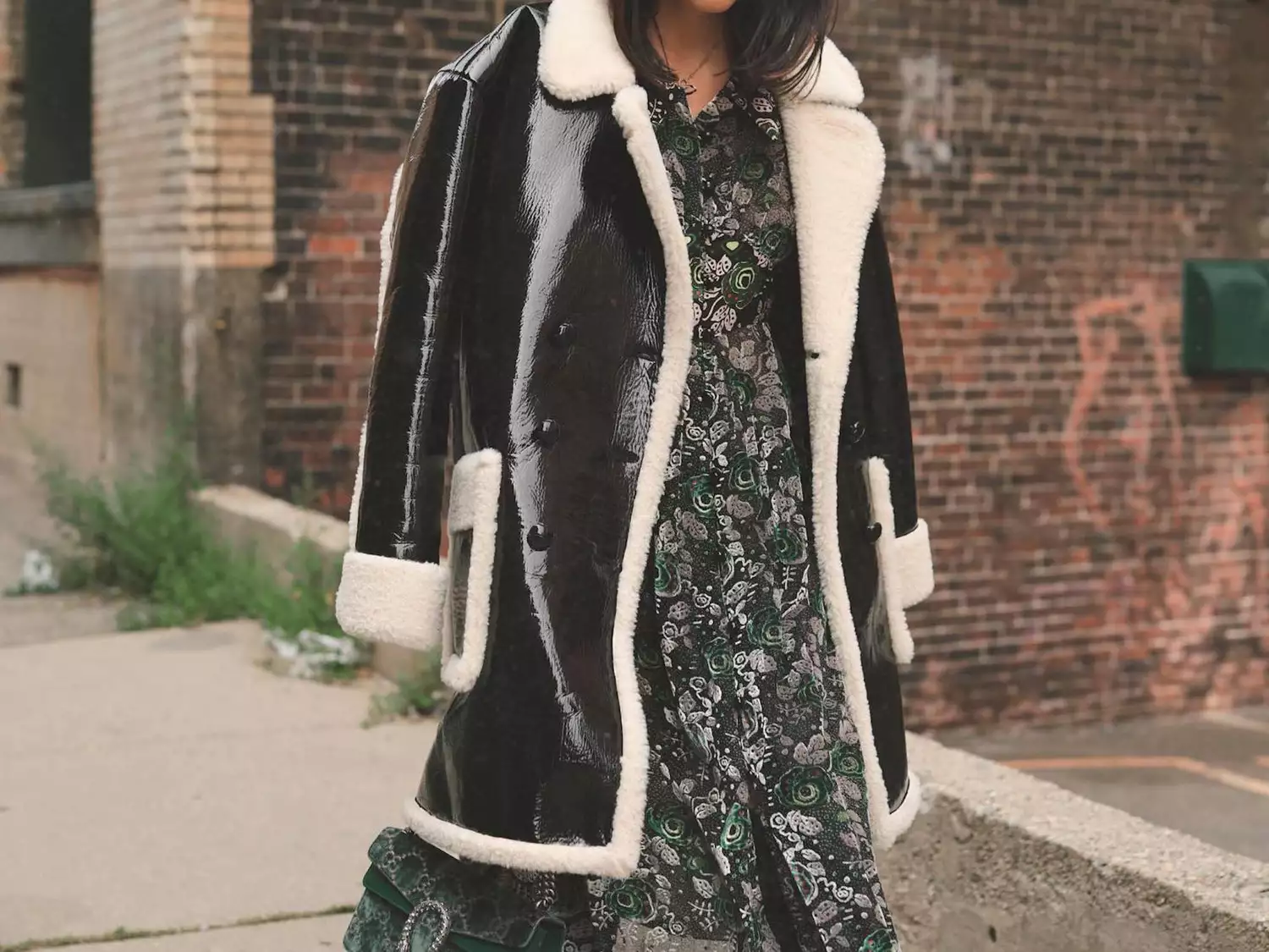 Byrdie writer Samantha Crompton wears a shearling-lined pleather coat over a patterned midi dress