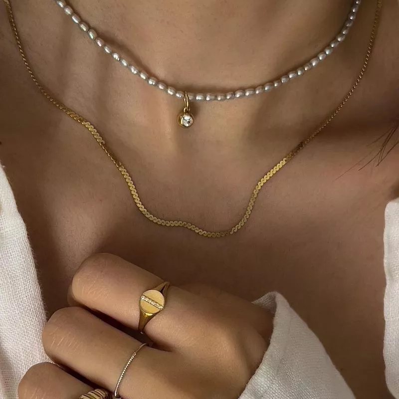 Woman wearing minimalist pearl and gold necklaces and rings