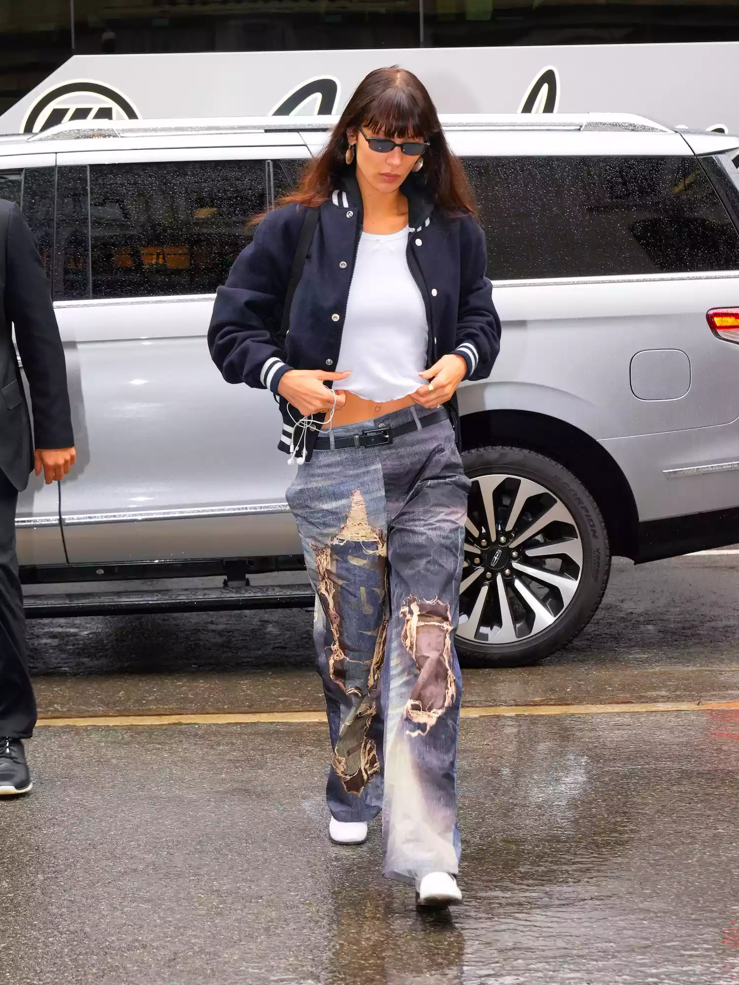 Bella Hadid wears a varsity jacket, white t-shirt, and ripped jeans