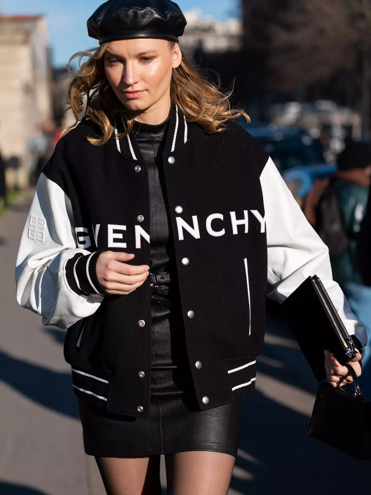 Woman wears black and white Givenchy varsity jacket, black mini dress, clutch, and beret