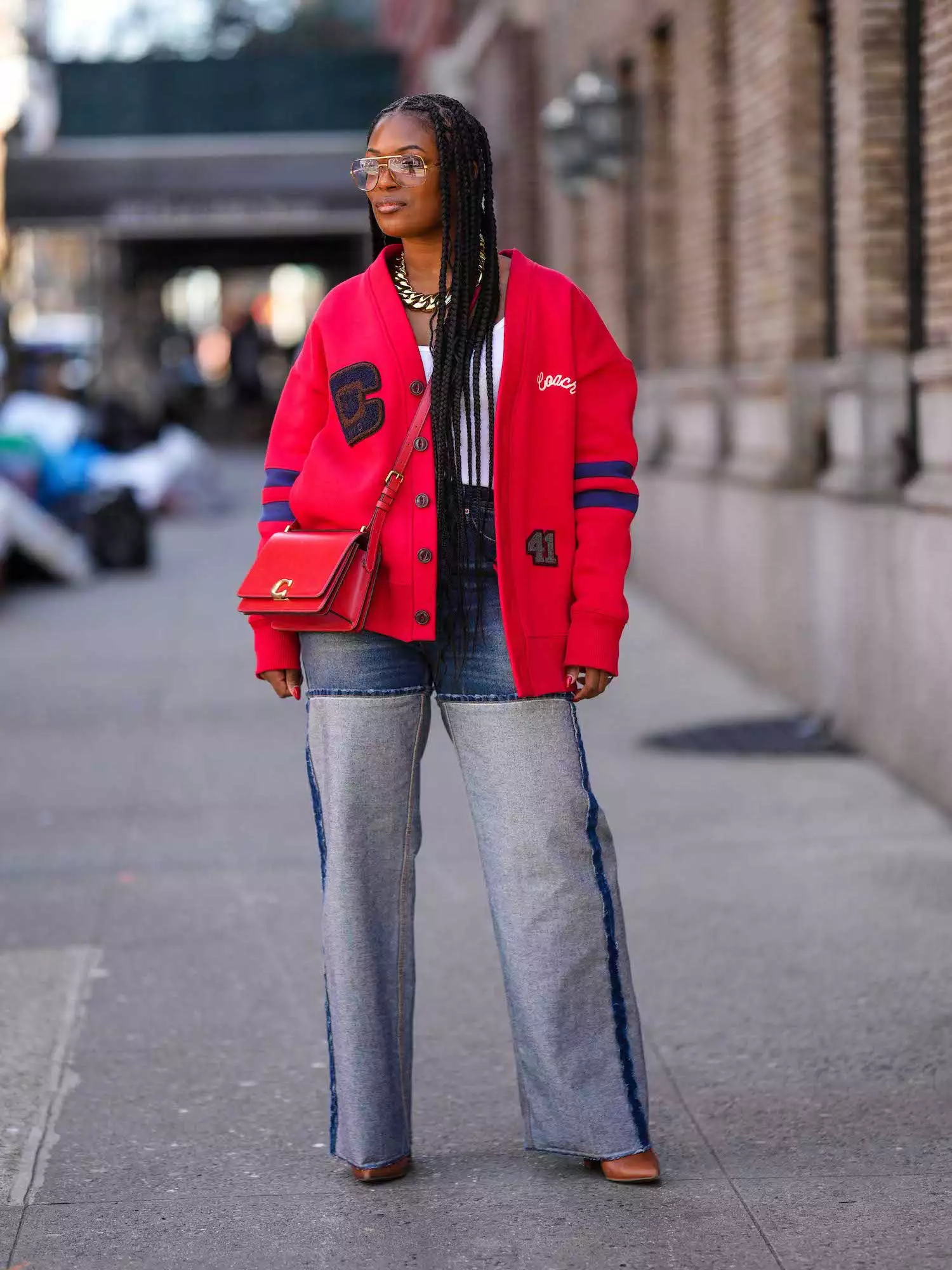 Woman wearing red Coach varsity jacket, purse, wide-leg jeans, and sunglasses