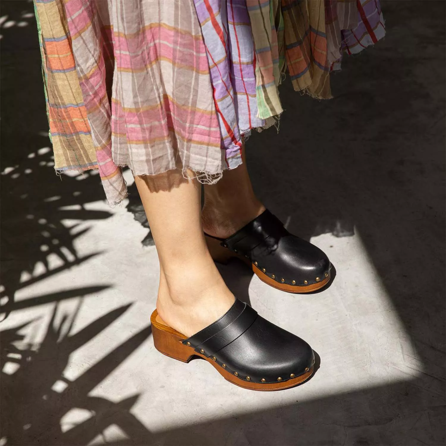 Model wearing black clogs and a plaid skirt.